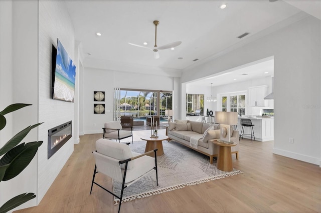 living area with recessed lighting, a fireplace, light wood-type flooring, ornamental molding, and baseboards