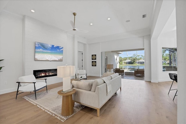 living area featuring a glass covered fireplace, wood finished floors, baseboards, crown molding, and recessed lighting