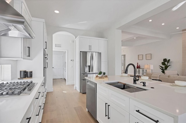 kitchen with wall chimney range hood, stainless steel appliances, a sink, light wood finished floors, and white cabinetry