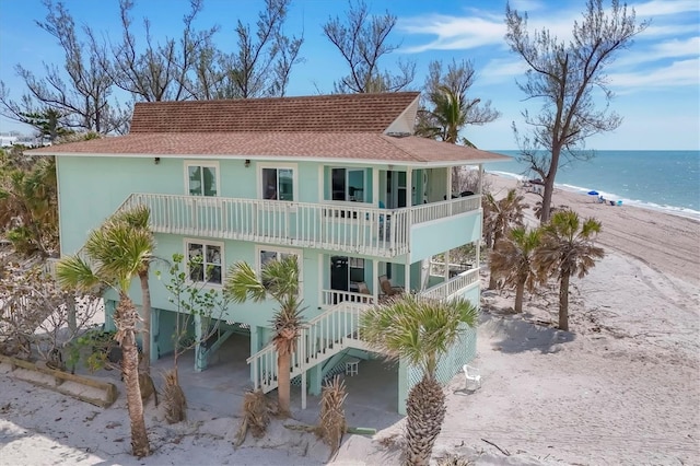 back of property featuring a beach view, a water view, driveway, stairway, and a carport