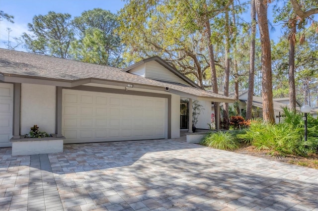 view of front of house with a garage, decorative driveway, roof with shingles, and stucco siding