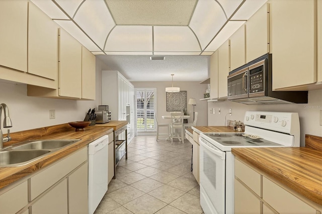 kitchen with a sink, white appliances, cream cabinets, and wood counters