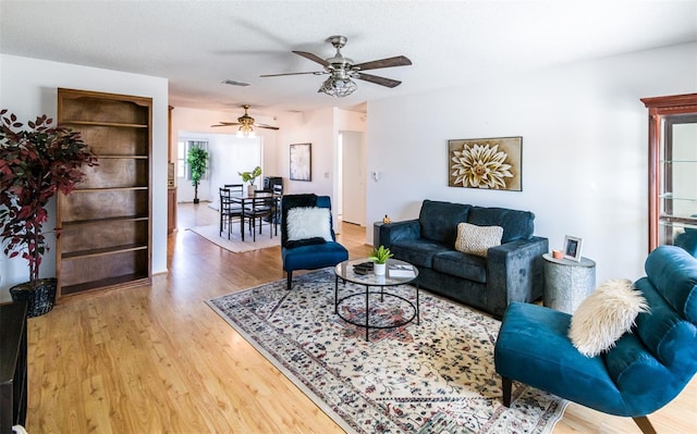 living area featuring a ceiling fan, visible vents, a textured ceiling, and wood finished floors