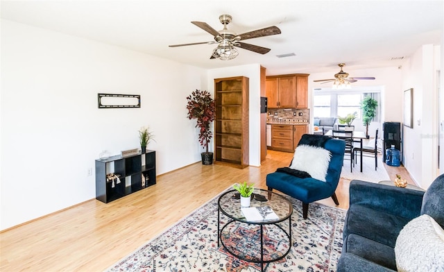 living room featuring light wood-style flooring, visible vents, and a ceiling fan