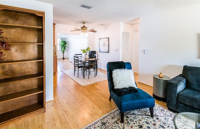 living area featuring a ceiling fan, visible vents, light wood-style flooring, and a textured ceiling