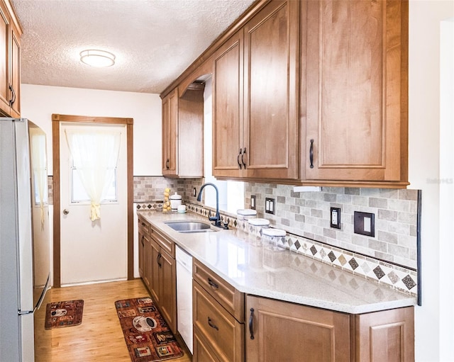 kitchen with white dishwasher, a sink, light countertops, freestanding refrigerator, and light wood finished floors