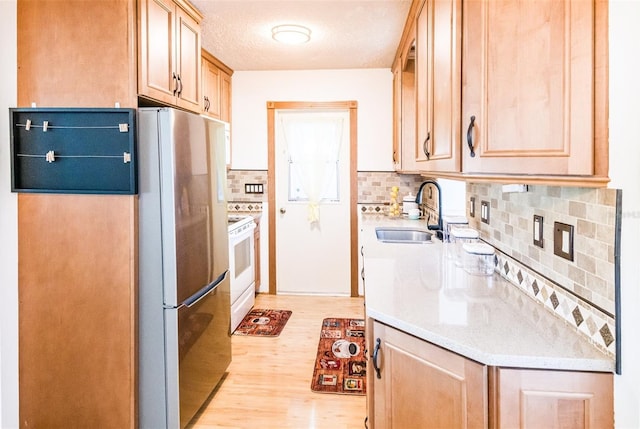 kitchen with a sink, light wood-style floors, light countertops, freestanding refrigerator, and white range with electric cooktop