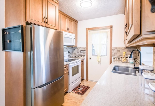 kitchen featuring light wood-style flooring, backsplash, a sink, a textured ceiling, and white appliances