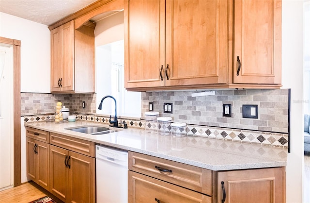 kitchen featuring white dishwasher, a sink, decorative backsplash, light stone countertops, and light brown cabinetry