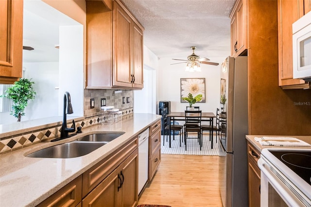 kitchen featuring tasteful backsplash, a sink, light stone countertops, light wood-type flooring, and white appliances