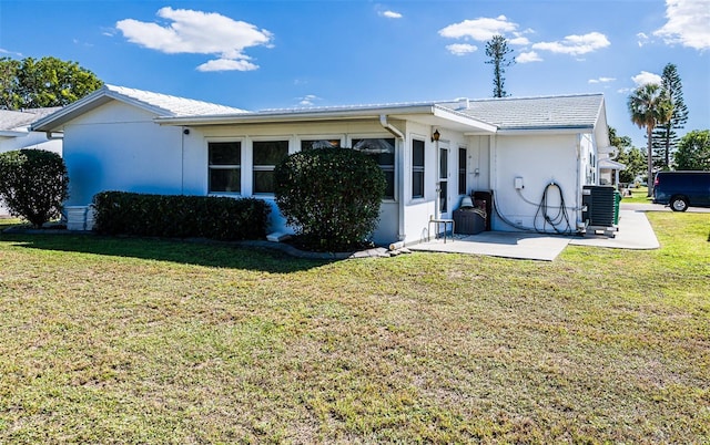 rear view of house with stucco siding, central AC unit, a lawn, and a patio