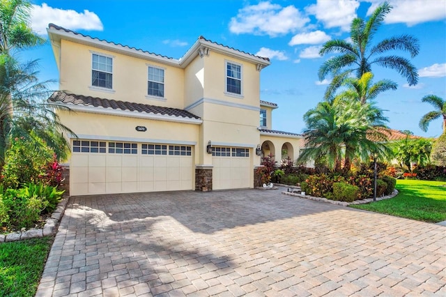 mediterranean / spanish house with an attached garage, a tile roof, stone siding, decorative driveway, and stucco siding