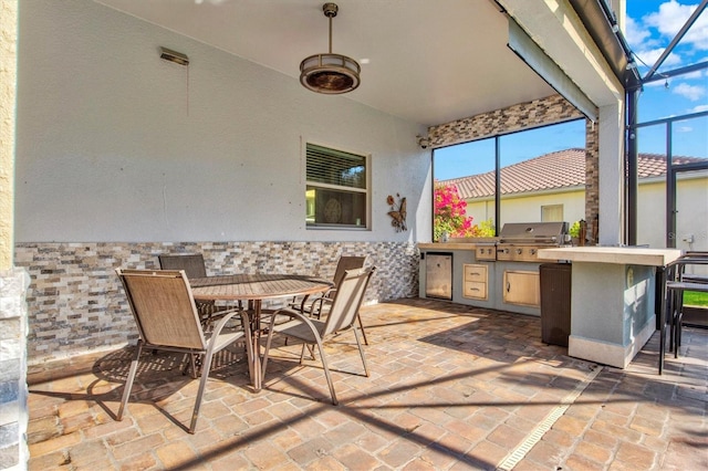 view of patio with glass enclosure, exterior kitchen, area for grilling, and outdoor dining space