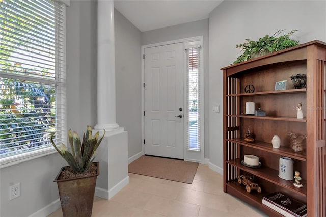 entryway with light tile patterned floors, plenty of natural light, decorative columns, and baseboards