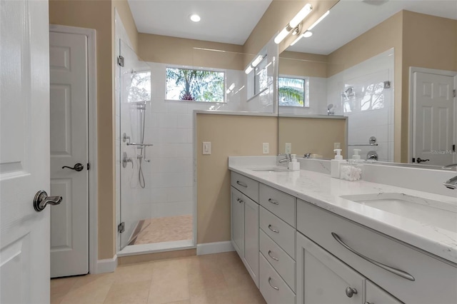 full bathroom with double vanity, baseboards, a walk in shower, and a sink