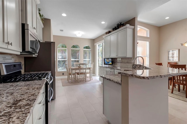 kitchen featuring light stone counters, recessed lighting, stainless steel appliances, a peninsula, and backsplash