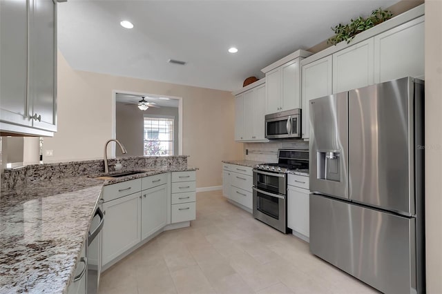 kitchen featuring decorative backsplash, light stone countertops, stainless steel appliances, a sink, and recessed lighting