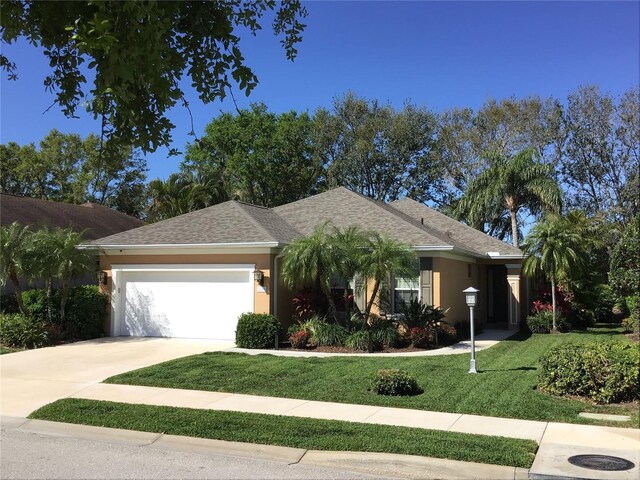 ranch-style house with concrete driveway, a front yard, roof with shingles, stucco siding, and a garage