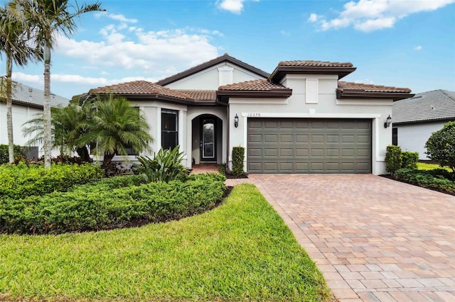 mediterranean / spanish house featuring an attached garage, a tiled roof, decorative driveway, and stucco siding