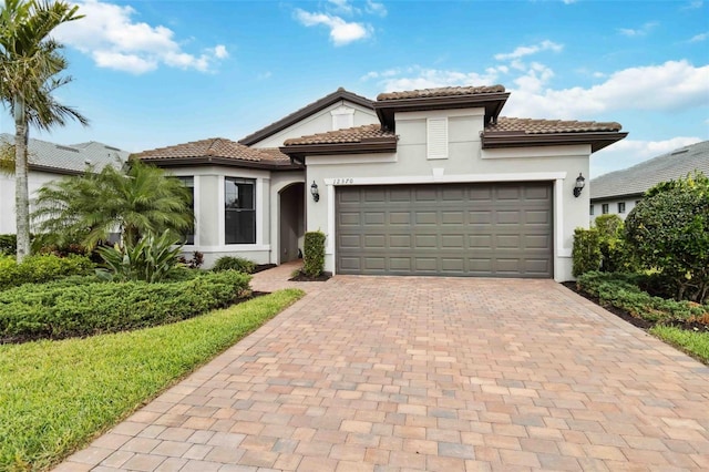 mediterranean / spanish house with a garage, decorative driveway, a tile roof, and stucco siding