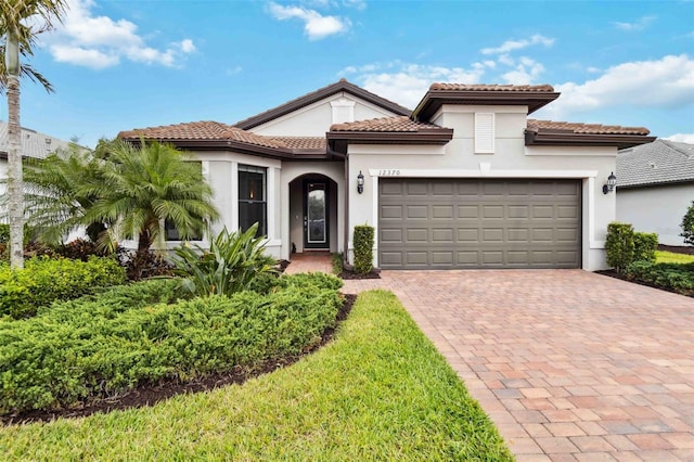 mediterranean / spanish home with an attached garage, a tile roof, decorative driveway, and stucco siding