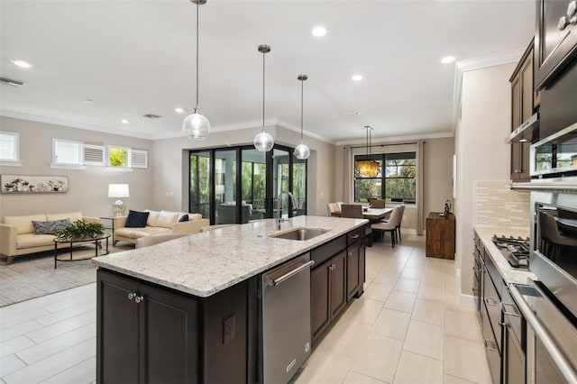 kitchen featuring tasteful backsplash, a center island with sink, appliances with stainless steel finishes, crown molding, and a sink