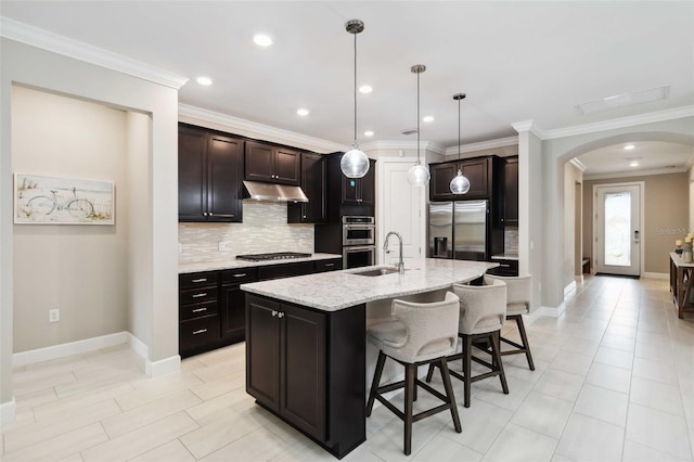 kitchen with arched walkways, a breakfast bar area, appliances with stainless steel finishes, a sink, and under cabinet range hood