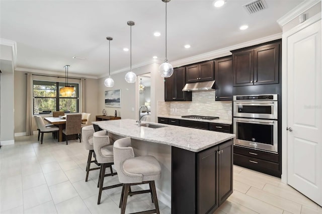 kitchen featuring under cabinet range hood, stainless steel appliances, a sink, visible vents, and backsplash