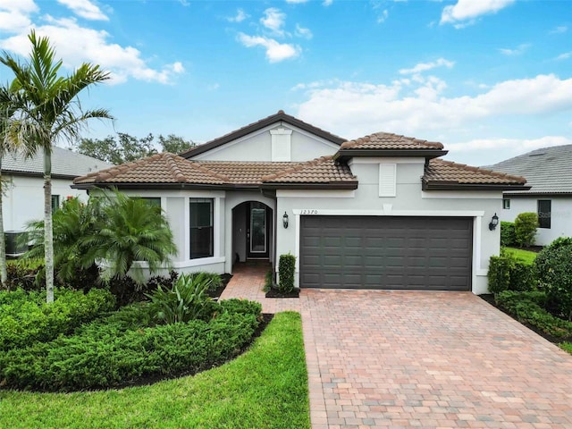 mediterranean / spanish house with decorative driveway, an attached garage, a tile roof, and stucco siding