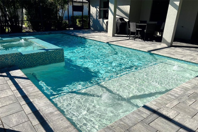 view of swimming pool featuring glass enclosure, a patio, a pool with connected hot tub, and grilling area