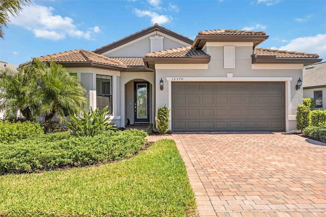 mediterranean / spanish house featuring stucco siding, an attached garage, a tile roof, and decorative driveway