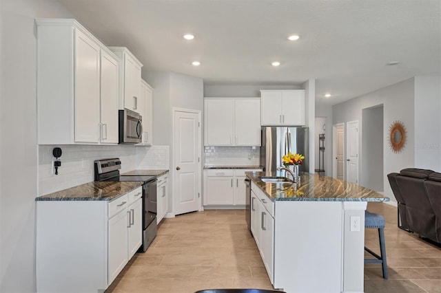 kitchen with dark stone counters, an island with sink, appliances with stainless steel finishes, open floor plan, and a kitchen bar