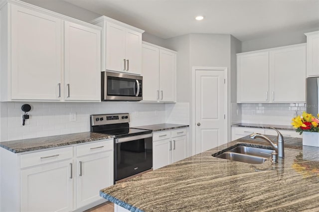 kitchen featuring decorative backsplash, appliances with stainless steel finishes, white cabinets, a sink, and dark stone countertops