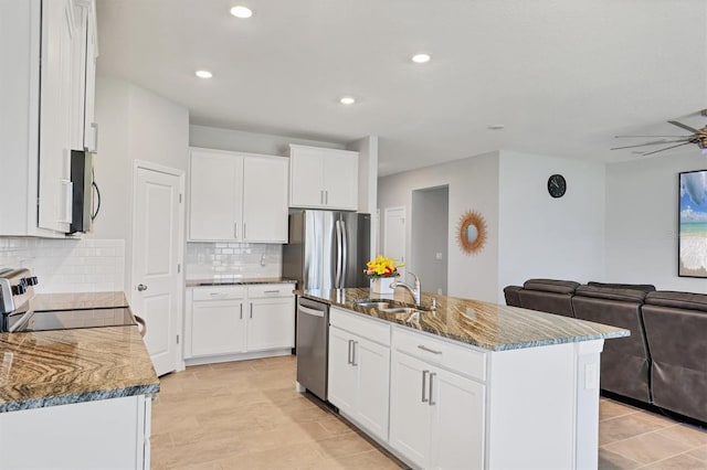 kitchen with a sink, a ceiling fan, open floor plan, appliances with stainless steel finishes, and dark stone counters