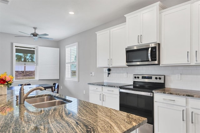 kitchen with appliances with stainless steel finishes, dark stone counters, a sink, and tasteful backsplash