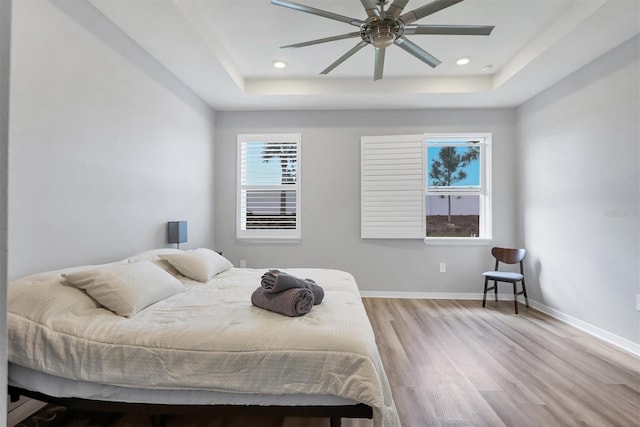 bedroom with a tray ceiling, recessed lighting, baseboards, and wood finished floors