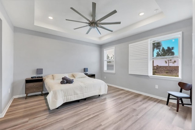 bedroom featuring wood finished floors, recessed lighting, a raised ceiling, and baseboards