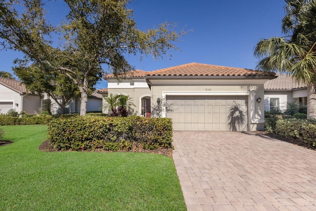 mediterranean / spanish house featuring a tiled roof, a front yard, stucco siding, decorative driveway, and a garage