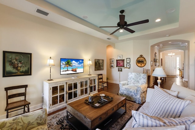 living area featuring arched walkways, visible vents, a tray ceiling, and wood finished floors