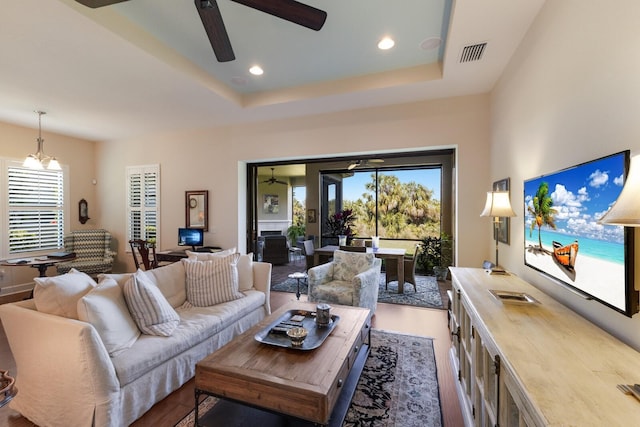 living area with visible vents, ceiling fan with notable chandelier, and a raised ceiling