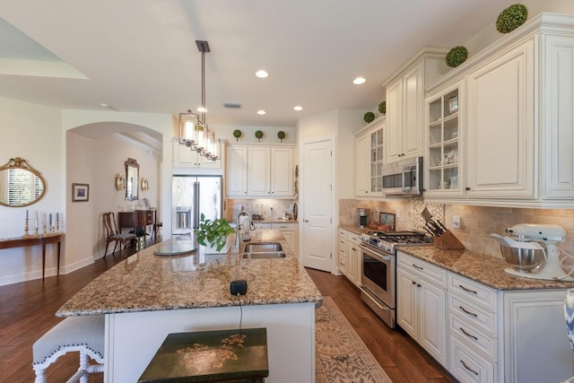 kitchen with dark wood-type flooring, a sink, arched walkways, appliances with stainless steel finishes, and decorative backsplash