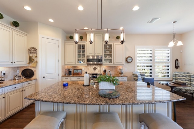 kitchen featuring dark wood-style floors, stone counters, a breakfast bar, recessed lighting, and stainless steel microwave