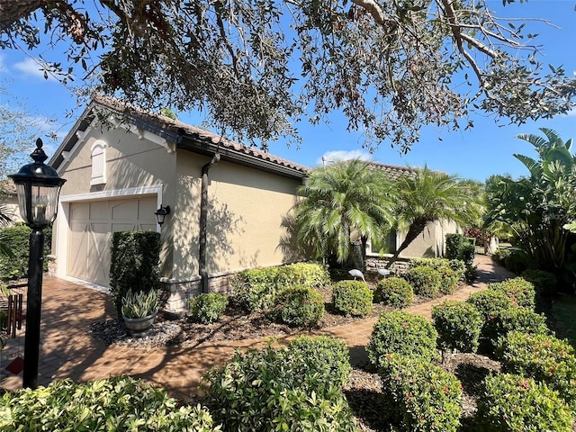 view of side of property with an attached garage, a tile roof, and stucco siding