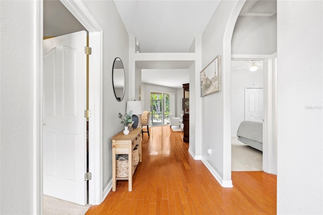 corridor featuring baseboards, arched walkways, visible vents, and light wood-style floors