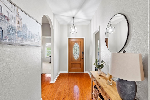 foyer entrance with arched walkways, a textured wall, baseboards, and wood finished floors