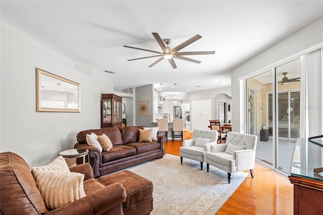 living area featuring a ceiling fan, arched walkways, visible vents, and light wood finished floors