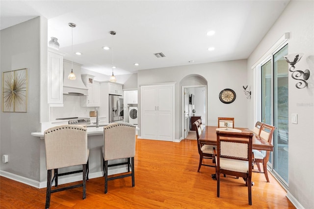 kitchen featuring arched walkways, a peninsula, stainless steel refrigerator with ice dispenser, and light wood-style floors