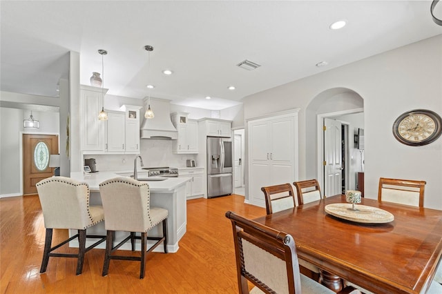 kitchen with a breakfast bar area, a peninsula, visible vents, stainless steel fridge with ice dispenser, and custom range hood