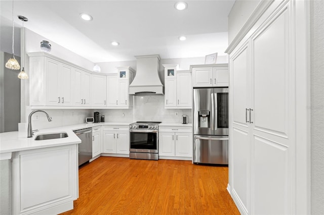 kitchen with premium range hood, a sink, appliances with stainless steel finishes, light wood-type flooring, and tasteful backsplash