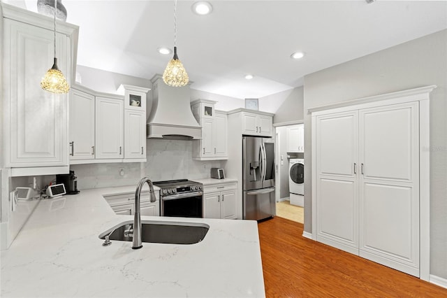 kitchen with decorative light fixtures, appliances with stainless steel finishes, a sink, washer / dryer, and premium range hood